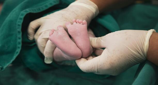Hände mit Handschuhen halten Baby-Füße.