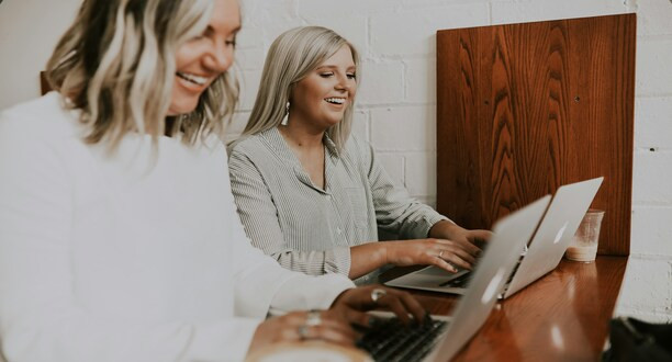 Zwei Frauen sitzen am Tisch am Laptop.