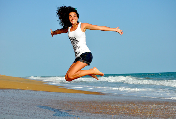 Frau springt an einem Strand in die Luft.